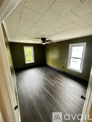 A room with a ceiling fan and two windows.