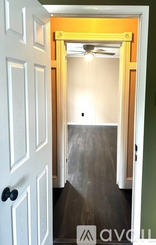 A white door with a black handle is open to a room with a ceiling fan.
