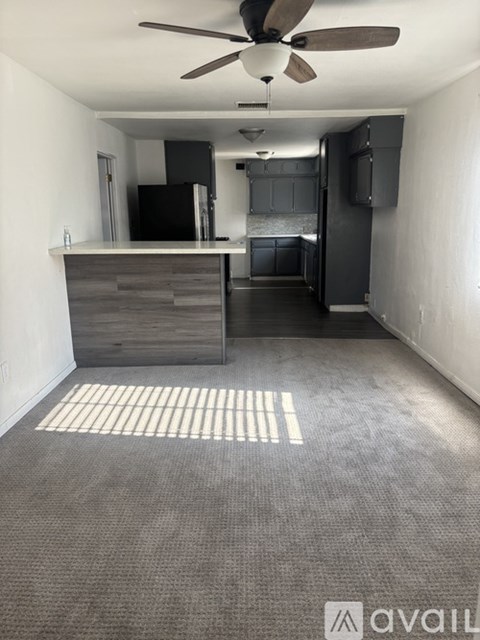 A room with a ceiling fan and a kitchen area with a counter and cabinets.