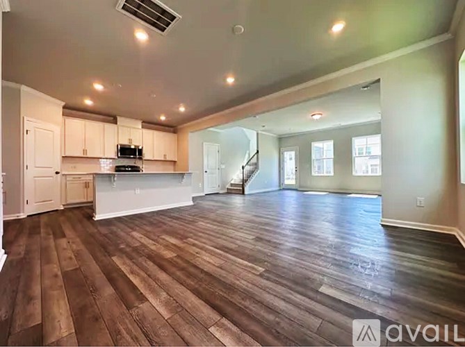 A spacious living room with hardwood floors and a staircase in the background.