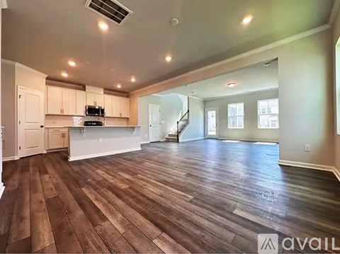A spacious living room with hardwood floors and a staircase in the background.