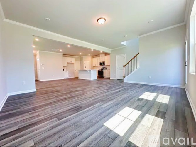 A spacious living room with wooden flooring and a staircase leading to another room.