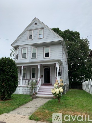 A white house with a front porch and a flower pot on the steps.