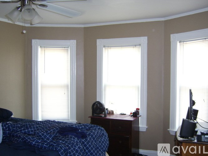 A bedroom with a bed, desk, and two windows.