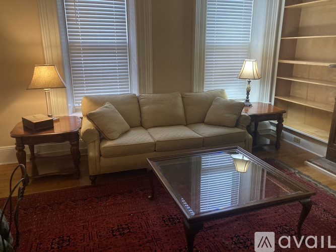 A living room with a beige couch, a glass table, and two lamps.