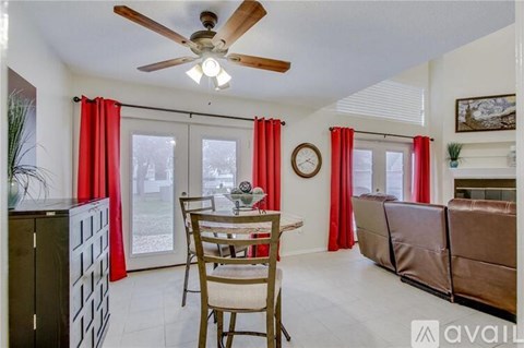 A living room with a dining table and chairs, a ceiling fan, and a window with red curtains.
