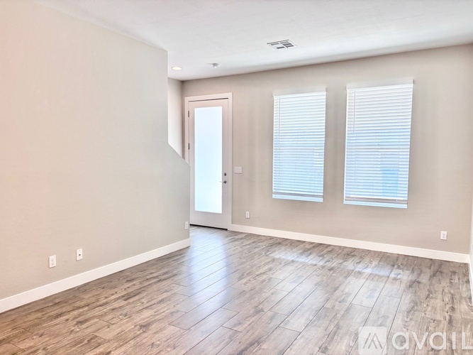 A spacious room with wooden flooring and a door leading to another room.