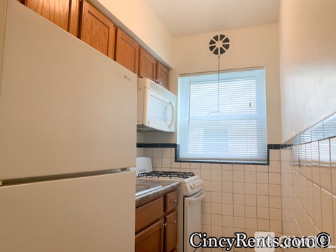 A kitchen with a white refrigerator and a window with blinds.