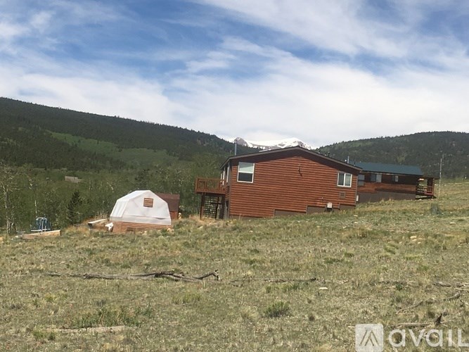 A small cabin sits in a grassy field with a mountain in the background.