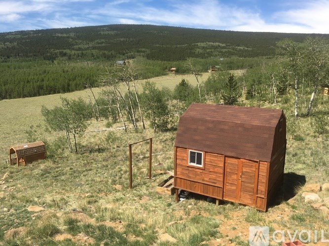 A small wooden shack sits in a grassy field with trees in the background.