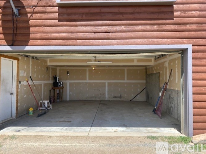 A garage with a white door is open and contains a broom, a mop, and a rake.