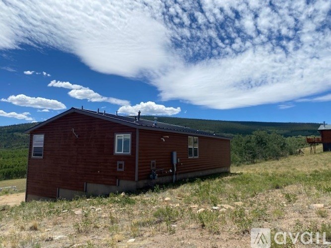 A red house with a white window and a brown door is situated in a grassy field.