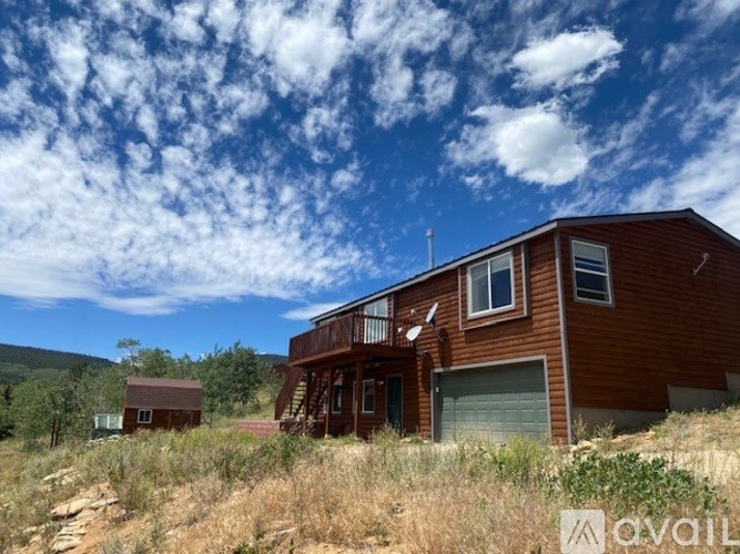 A large brown house with a balcony is in the foreground with a smaller house in the background.