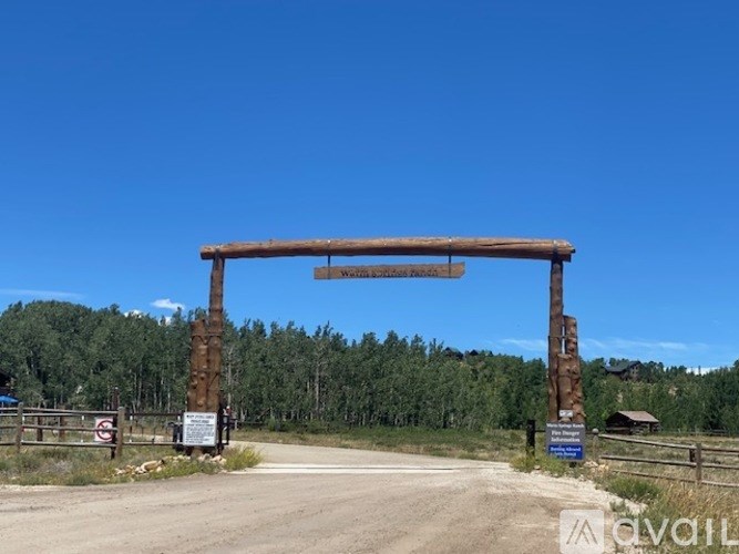 A wooden gate with a sign that reads "Welcome to Pine Forest" stands in front of a forest.
