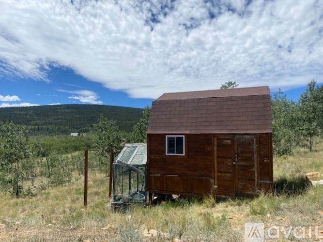 A small wooden shack with a metal roof and a door is situated in a grassy field.