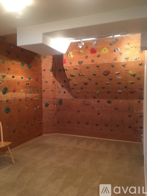 A climbing wall in a room with a wooden floor and a chair.