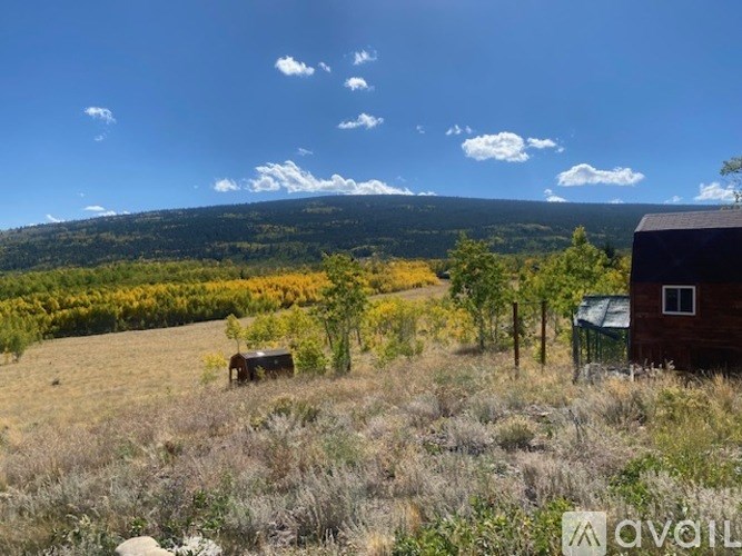 A rural landscape with a house, trees, and a mountain in the distance.