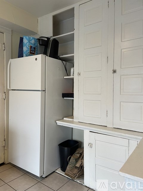 A white refrigerator with its door open and a black trash can underneath it.