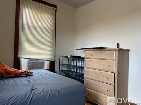 A bedroom with a bed, a dresser, and a window with blinds.