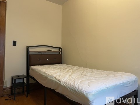 A bed with a white mattress and a wooden headboard is in a room with a white wall and a small black nightstand.