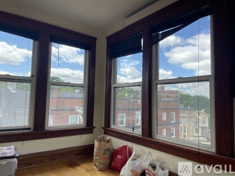 A room with brown windows and a white couch with bags on it.