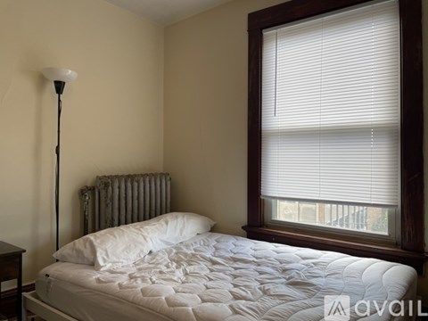 A bedroom with a white bed and a window with blinds.