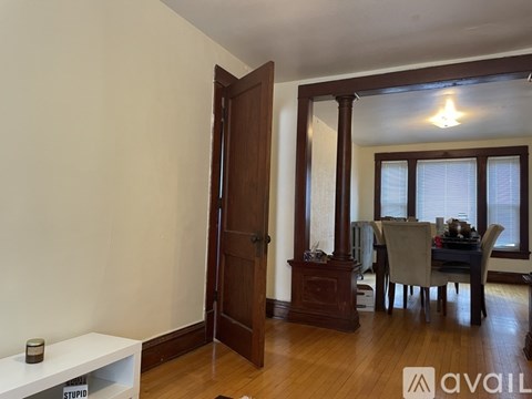 A room with a wooden floor and a white wall with a door and a table with chairs.