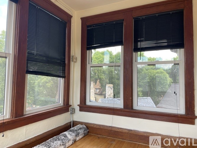 A room with two windows, one with blinds and a view of a house.
