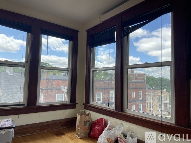 A room with brown windows and a white couch with bags on it.