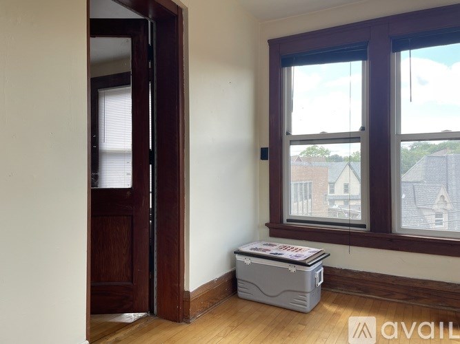 A room with a wooden door and a window with a view of houses outside.