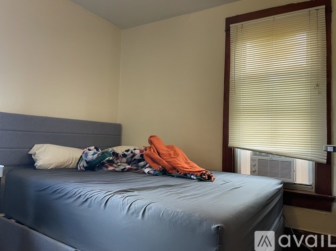 A bed with a blue sheet and a white pillow with a window behind it.