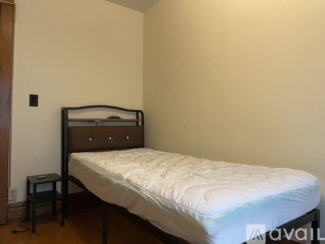 A bed with a white mattress and a wooden headboard is in a room with a white wall and a small black nightstand.