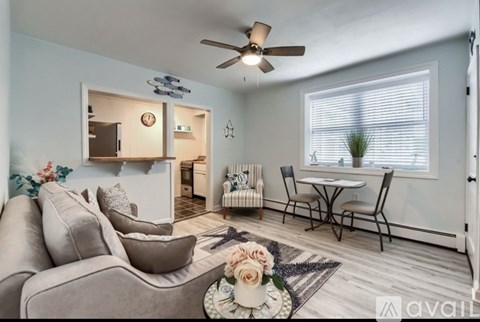 A living room with a grey sofa, a small table with chairs, and a ceiling fan.