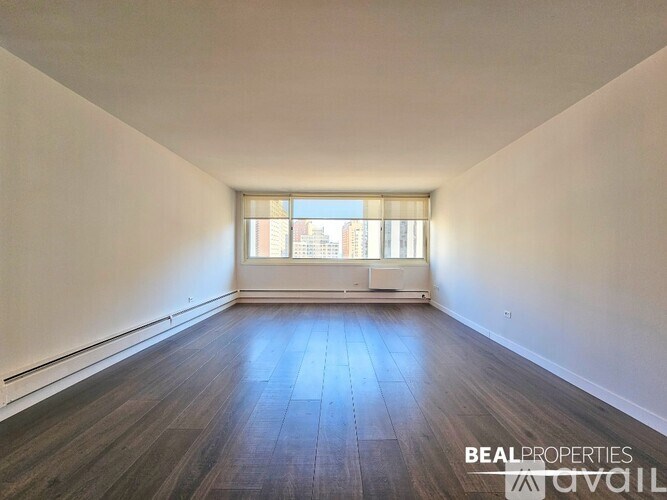 A spacious room with wooden flooring and a window letting in natural light.
