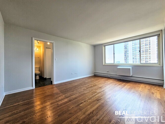 A spacious room with wooden flooring and a large window.