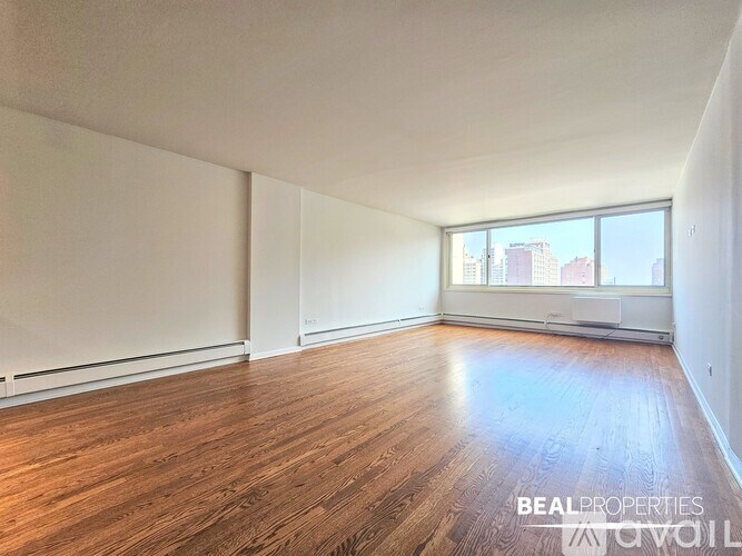 A spacious room with wooden flooring and a large window overlooking a cityscape.