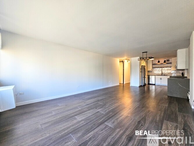 A spacious room with wooden flooring and a kitchen area in the background.