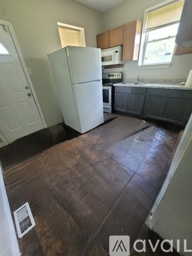 A kitchen with a white fridge and brown floor.