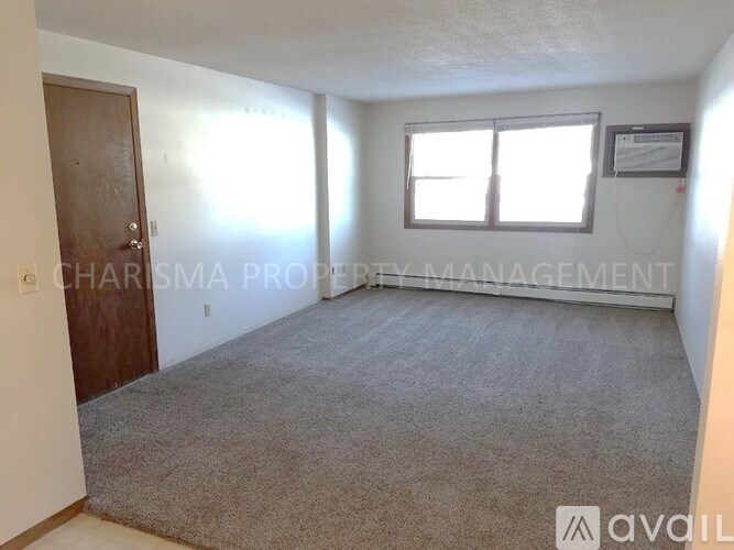 A room with a carpeted floor, a window with blinds, and a door.