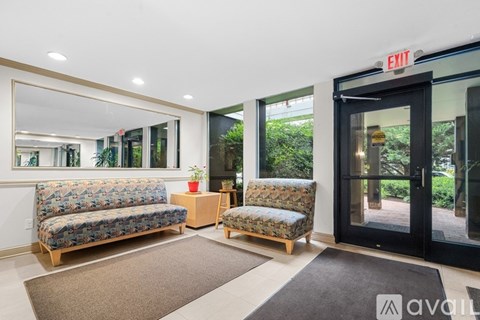 A living room with a couch, chair, and a rug in front of a door with an exit sign.