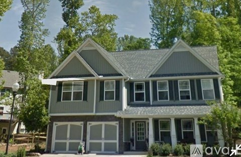 A two-story house with a garage is surrounded by trees.