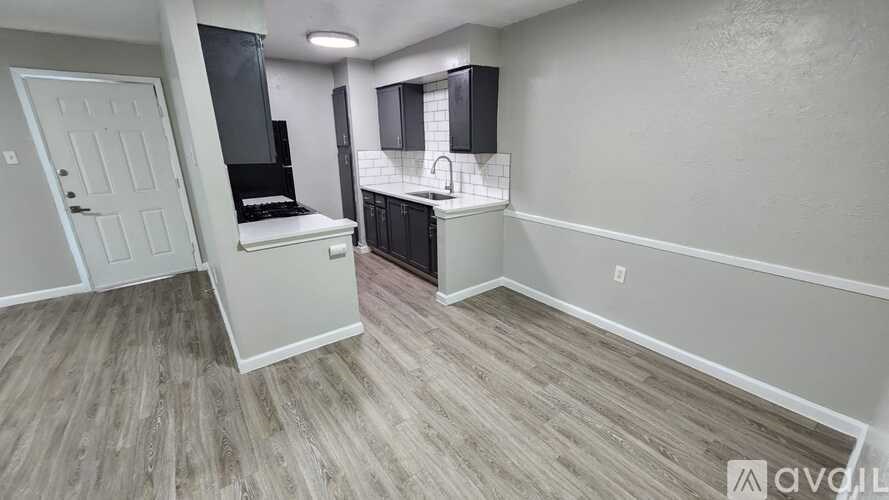 A room with a white door and a kitchenette with a sink and stove.