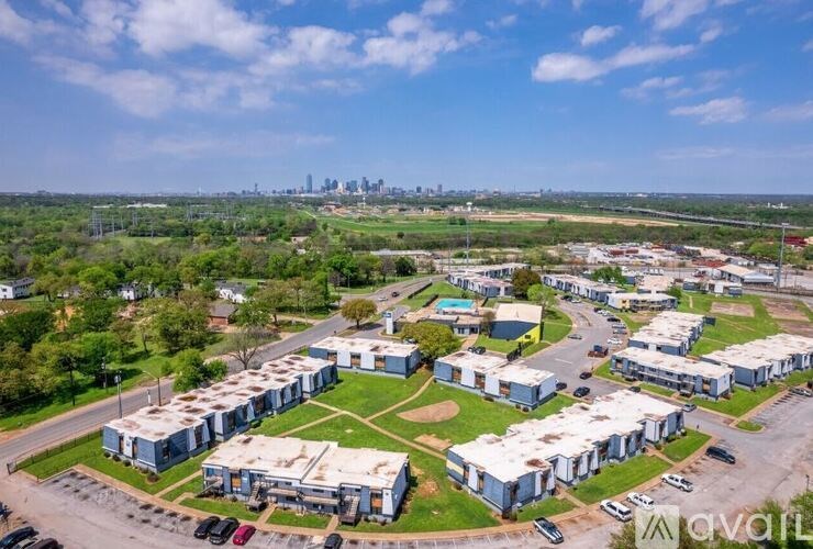 A large building complex with a parking lot in front and a city skyline in the distance.