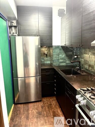 A kitchen with a stainless steel refrigerator and black countertops.