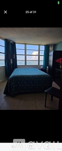 A bedroom with a bed, chair, and a window overlooking the ocean.