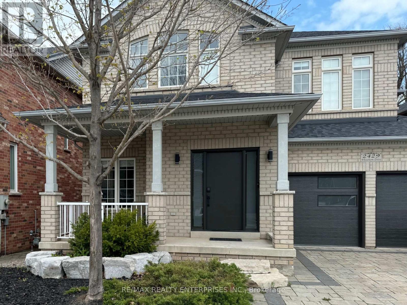 A house with a black front door and a tree in front.