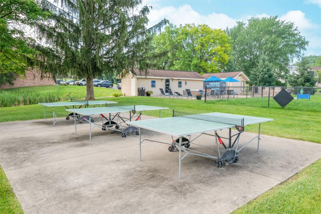 two ping pong tables in a park next to a tennis court