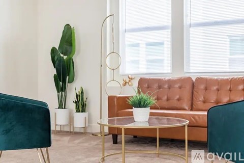 A living room with a brown leather couch, a green chair, and a glass table with a plant on it.