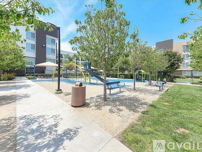 A sunny day at the park with a playground and a building in the background.