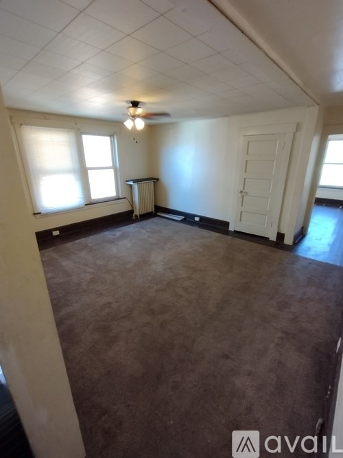 A room with a carpeted floor, a ceiling fan, and a door.